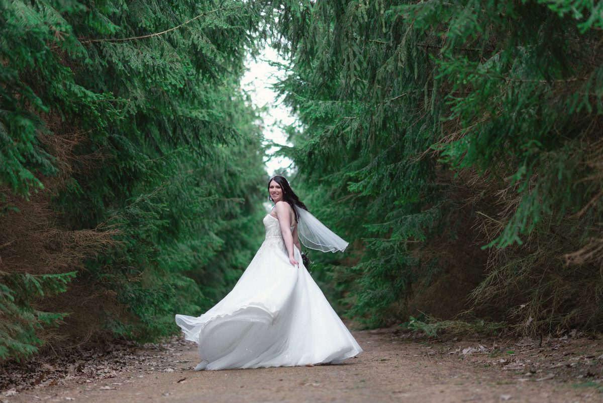Bride with her veil flowing behind her in a green tunnel of evergreens