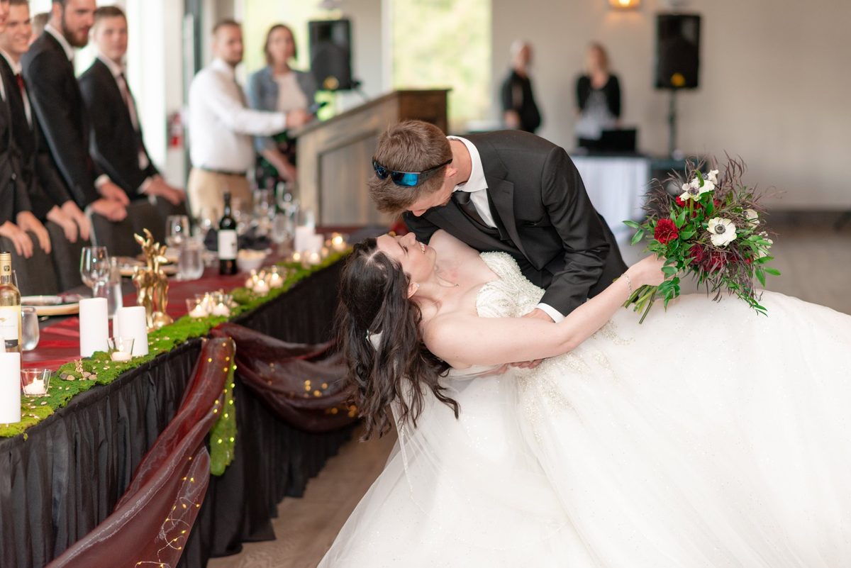 Groom dipping the bride for a kiss across the head table as the wedding party watches at Links of Kent