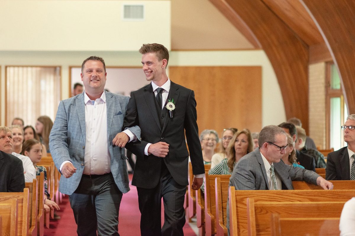 Groom walking down the church aisle with a family member as guests look on