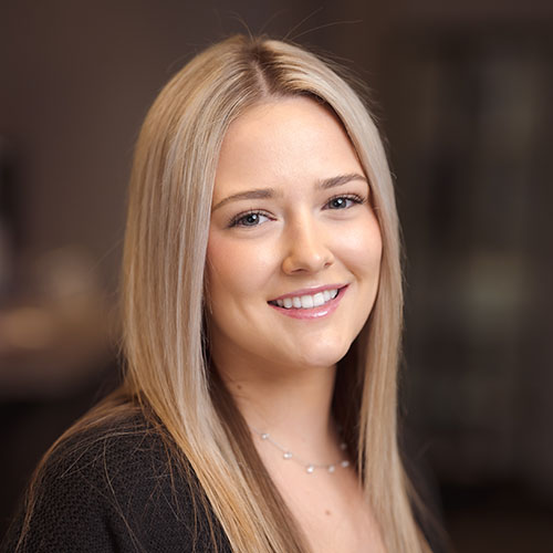 Smiling woman with long blonde hair and a dark top, an in-office team headshot with a warm, softly blurred background for a Chatham-Kent business