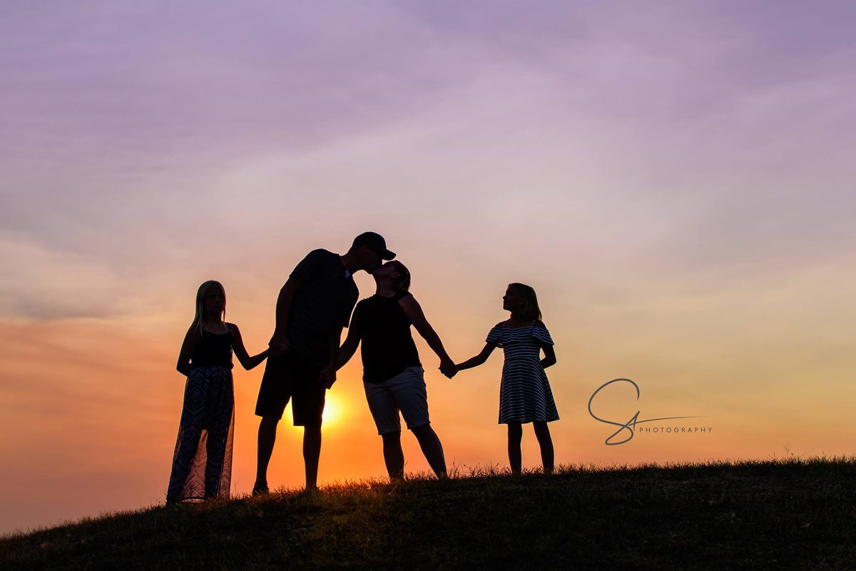 Silhouette of a family of four holding hands on a hill at sunset