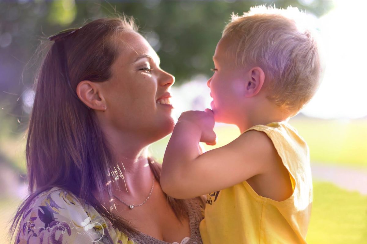 Mom and her blond toddler nose to nose, backlit by warm sunlight