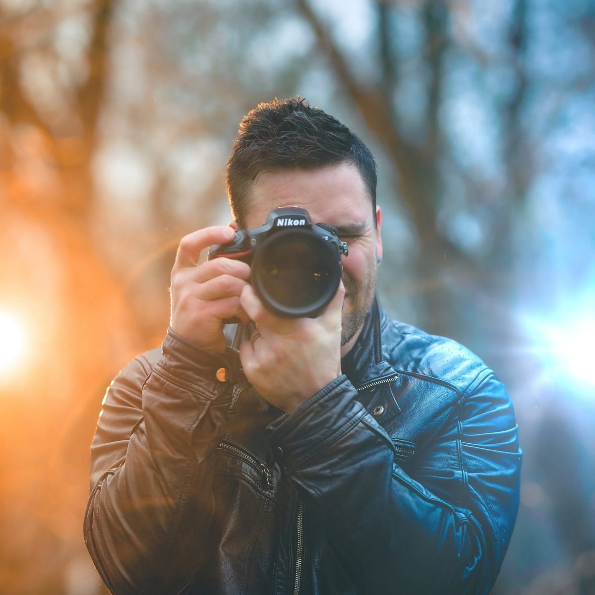 Steven Taylor raising his camera to take a photo, backlit by warm golden evening light through the trees