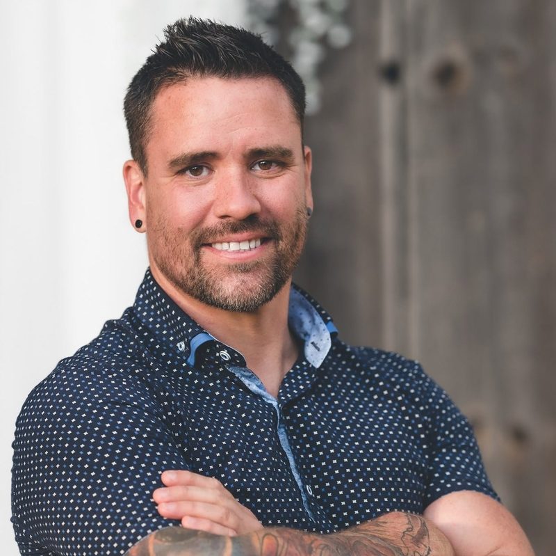 Steven Taylor, wedding photographer in Chatham-Kent and Windsor, smiling with his arms crossed in front of a rustic barn door